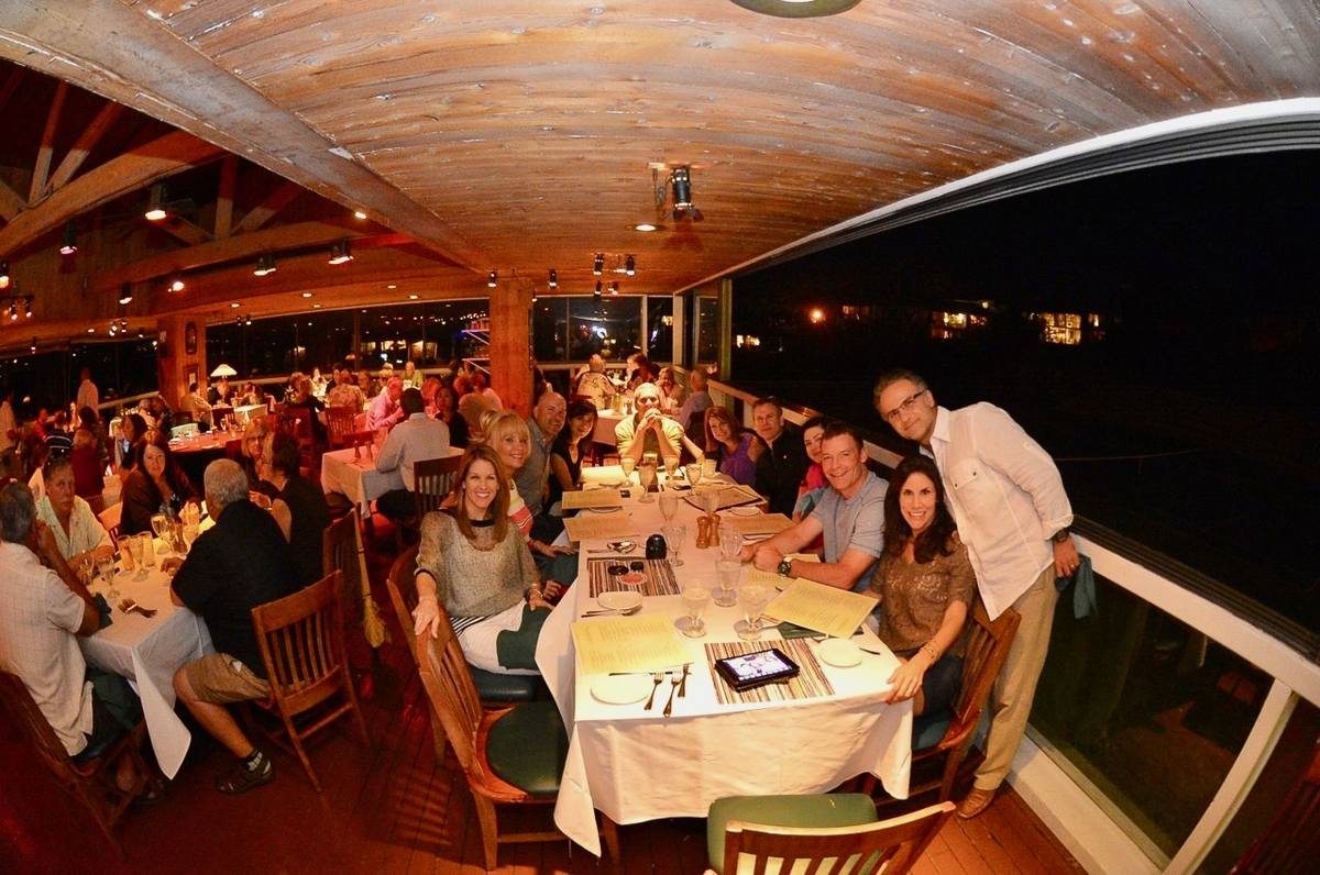 Long dinner tables on a timber-roofed lanai open to the bay at night