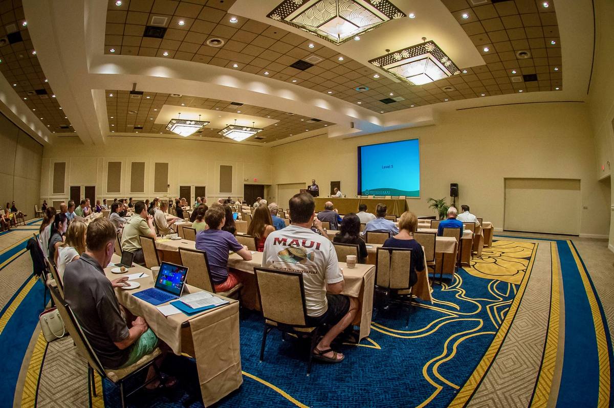 Attendees at classroom tables facing the screen in a ballroom on the Kona coast