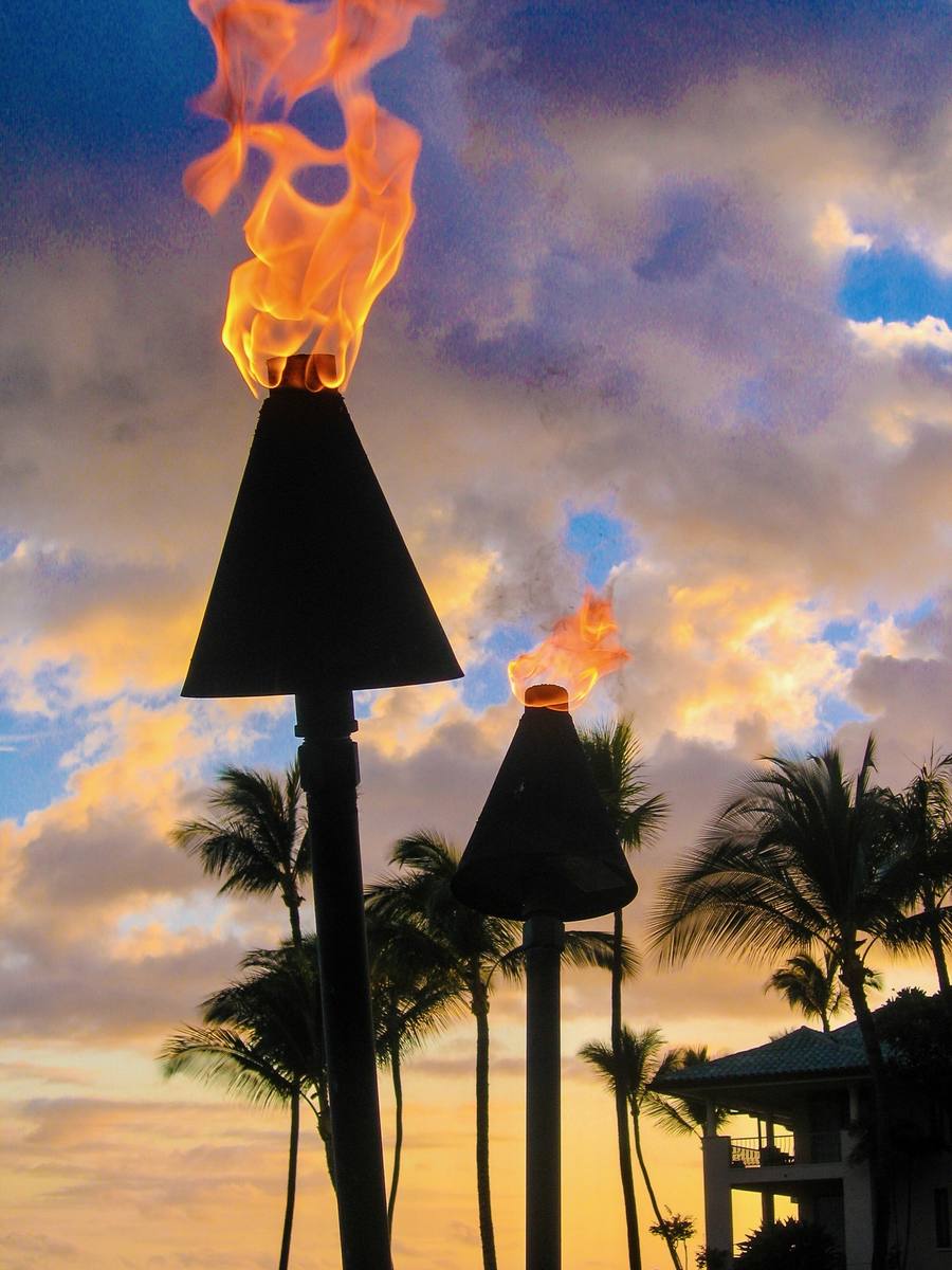 Tiki torches burning against a sunset sky and silhouetted palms
