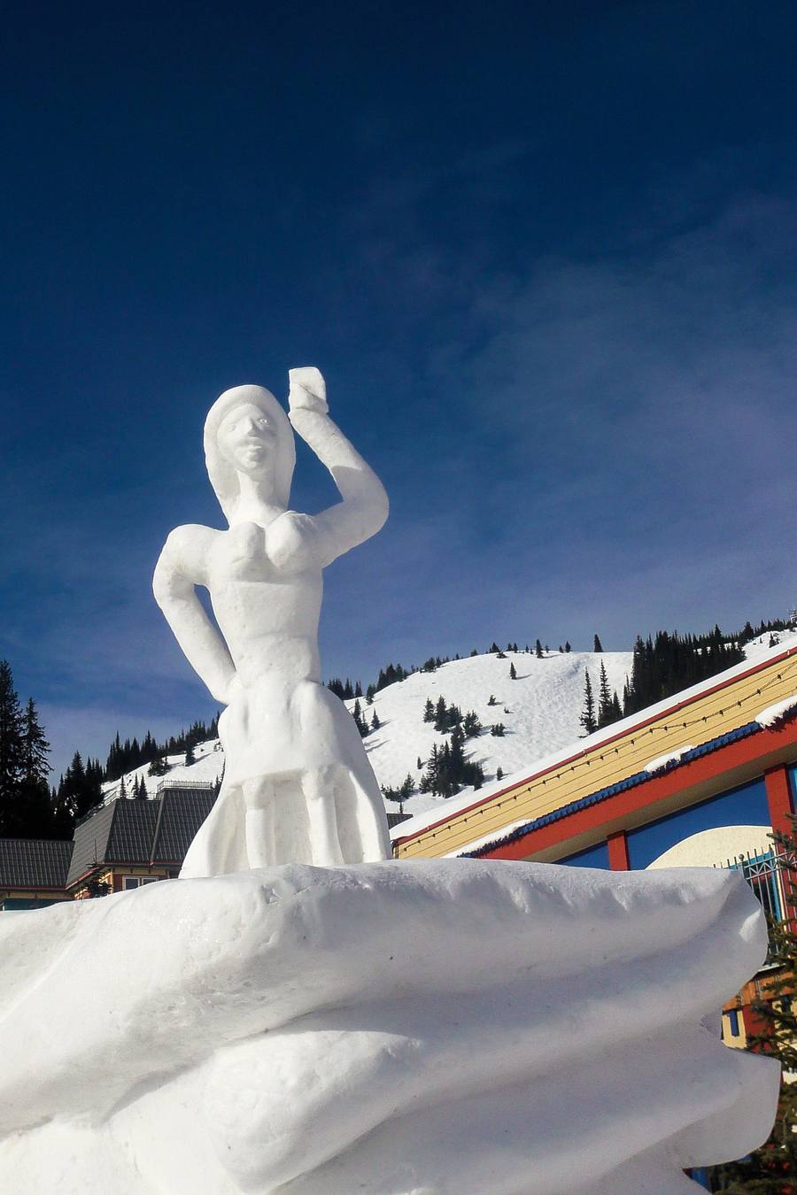 A snow sculpture of a figure shading its eyes, against a deep blue winter sky