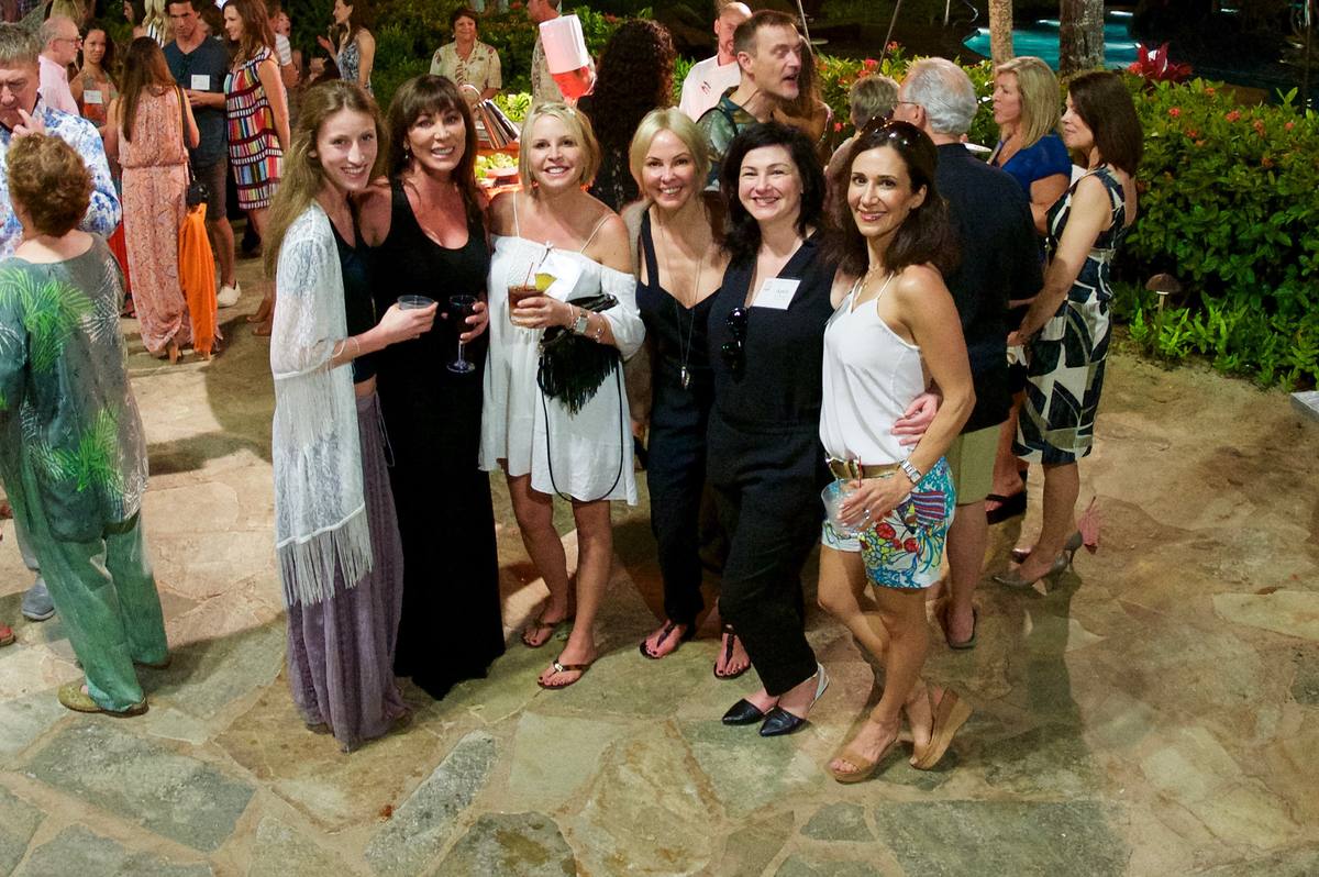 Guests at an evening reception on a stone terrace by the pool, tiki torches lit