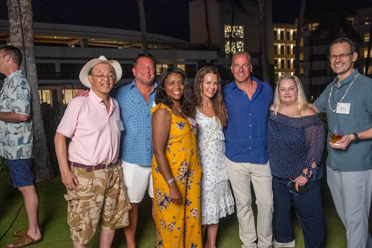 A group of members and partners together on the lawn at dusk, resort towers and palms behind