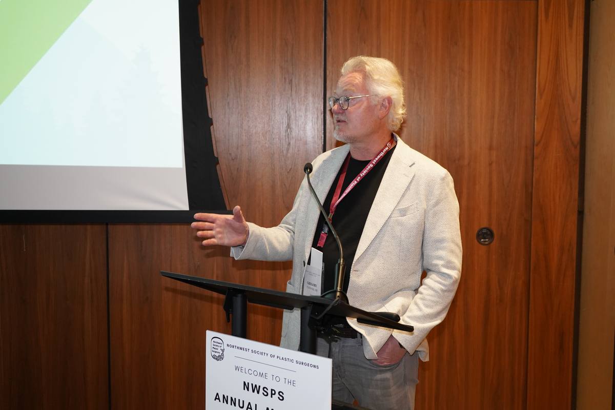 A lecturer gestures toward the screen while speaking from the lectern