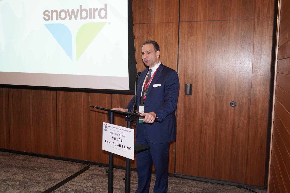 A speaker at the lectern with the Snowbird logo on the screen behind him in a wood-panelled meeting room