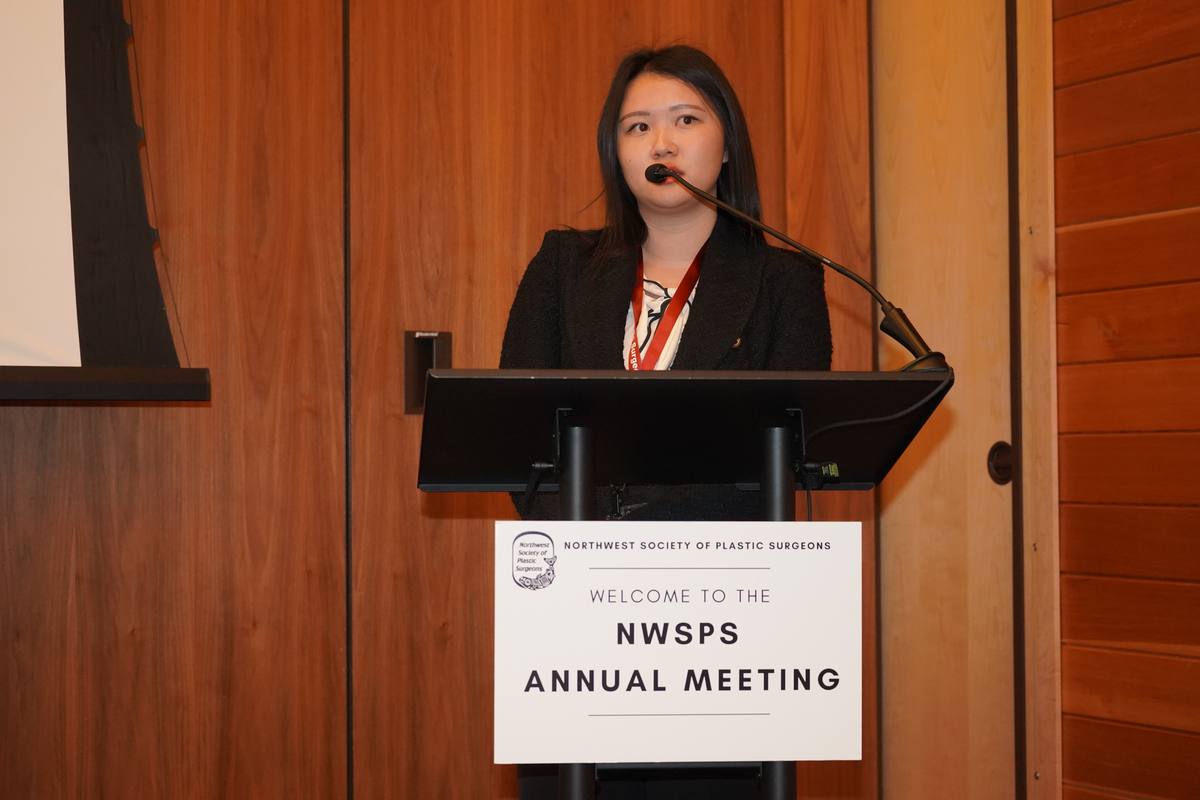 A presenter speaks at the lectern beneath the “Welcome to the NWSPS Annual Meeting” sign