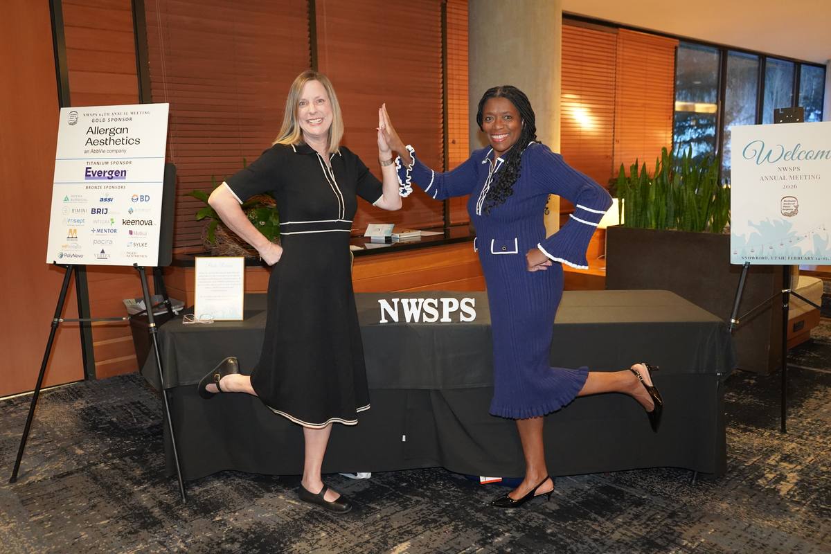 Two staff members strike a playful pose at the NWSPS registration desk beside the sponsor board