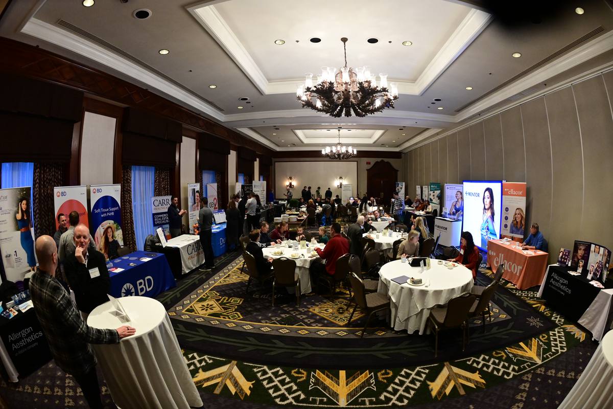A ballroom with breakfast tables in the centre and exhibitor booths and banners around the walls