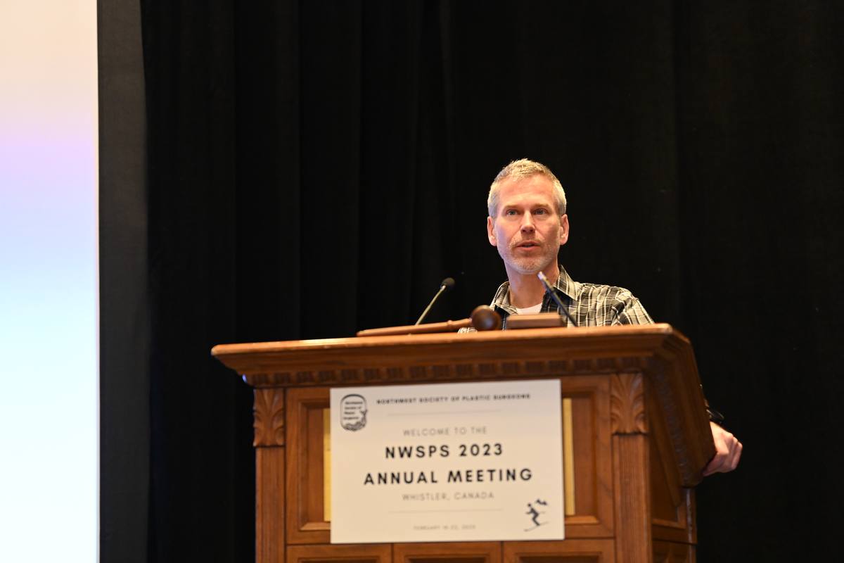 A speaker at the carved wooden lectern bearing the NWSPS 2023 Annual Meeting sign
