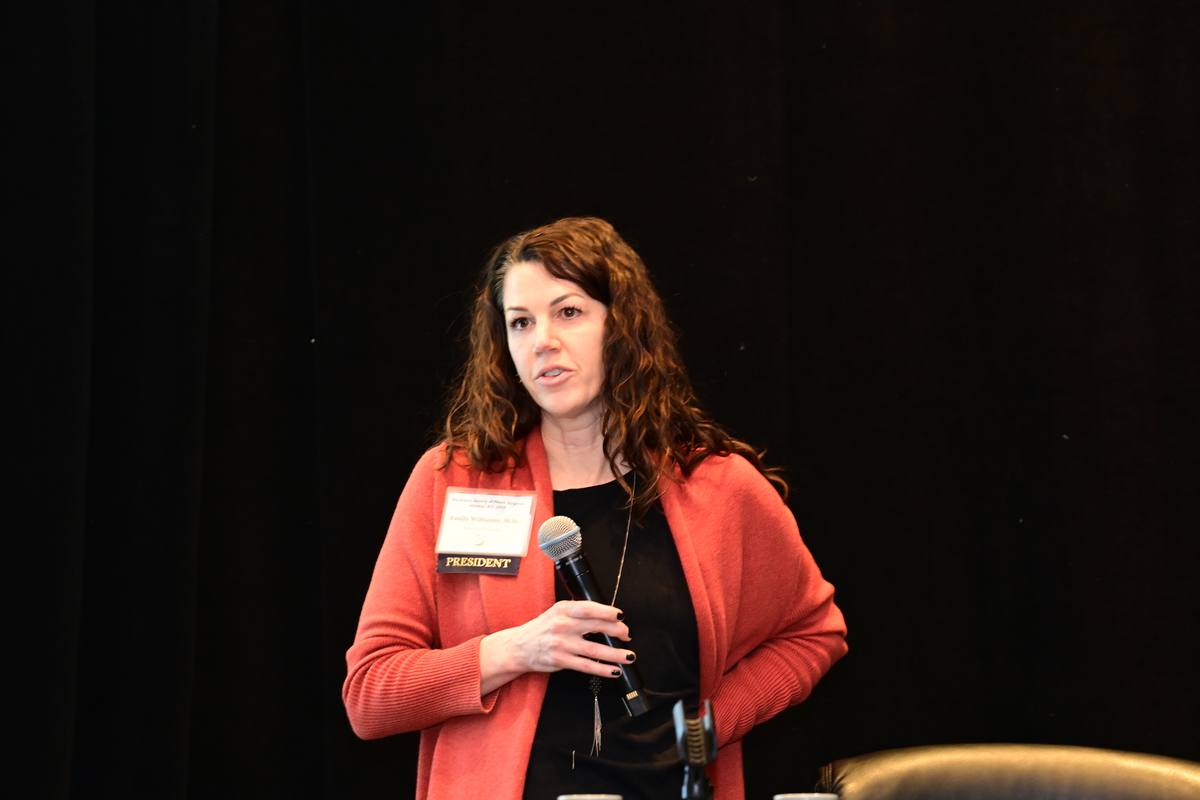 The Society’s president speaks into a microphone at the front of the darkened session room