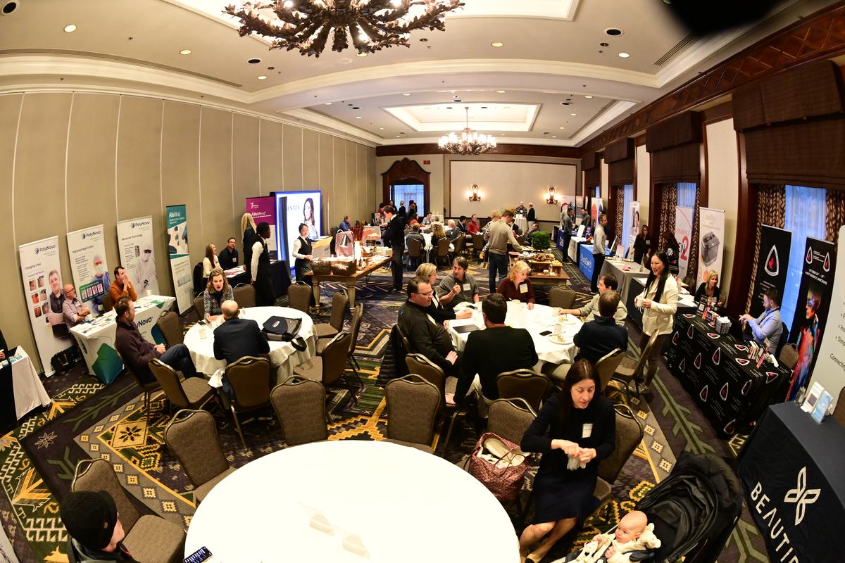 Attendees talk at round tables in the exhibit hall, booths and pull-up banners along the walls