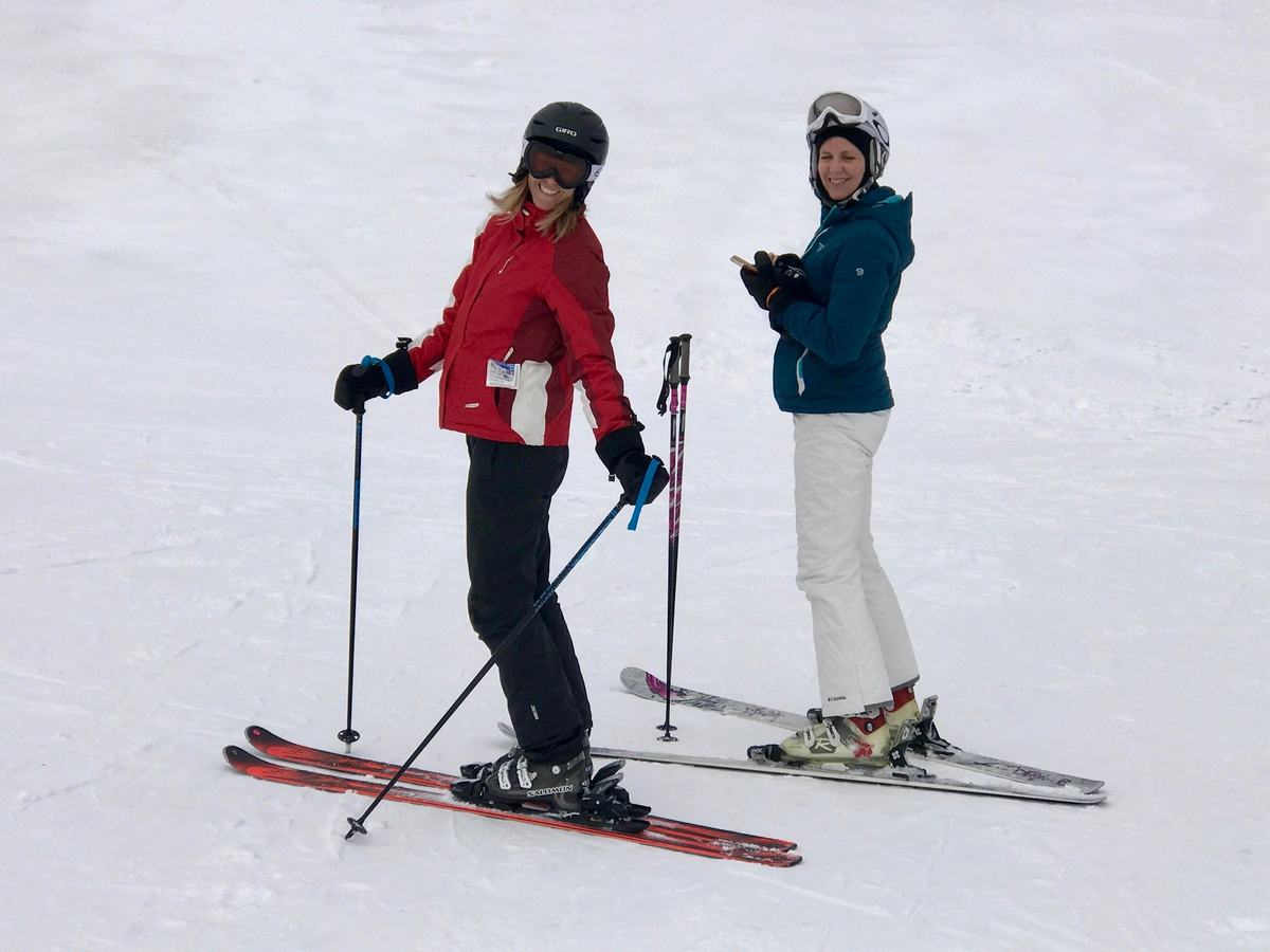 Two skiers in helmets pause on a wide, gentle slope of fresh snow