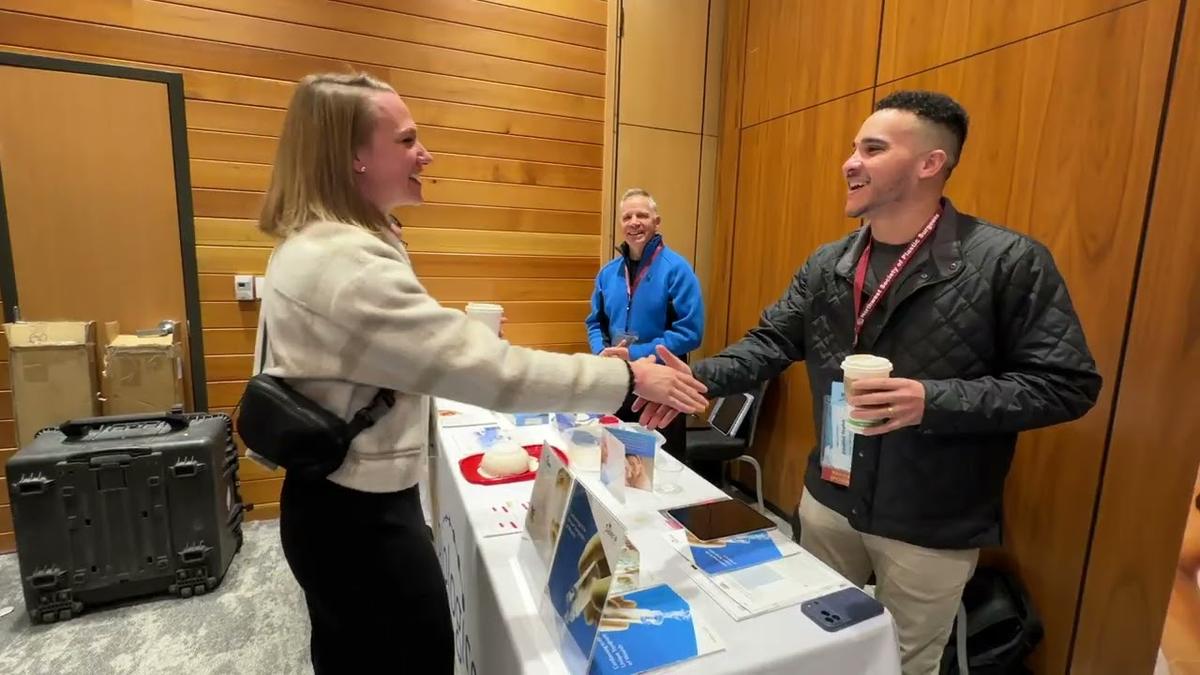A member and an exhibitor shake hands over a display table in the exhibit hall at Snowbird